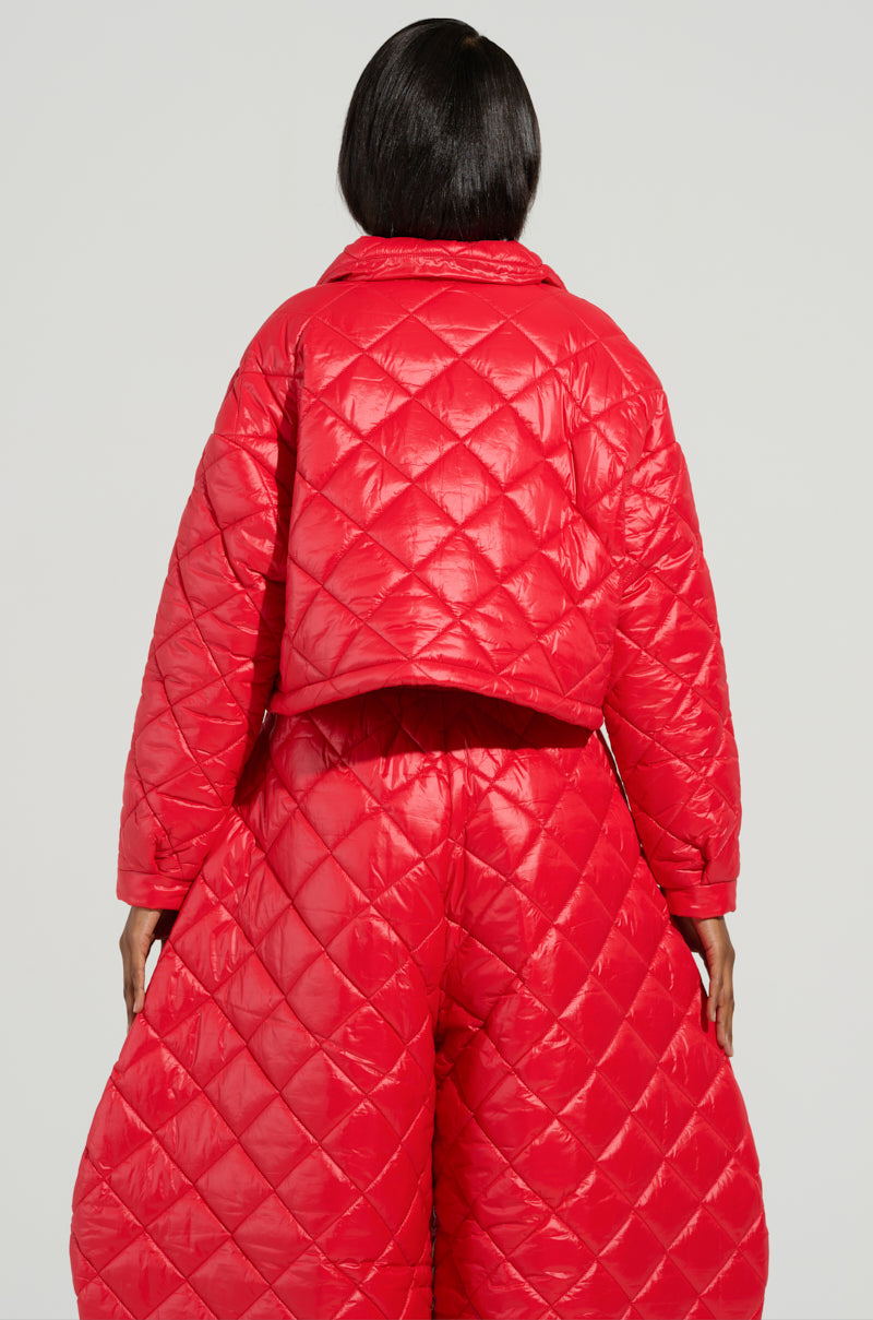 A person is wearing the VIVI Cropped Puffer Bomber in Red by AKIRA Label, styled with matching wide-legged pants. The diamond-quilted design, prominently displayed from the back, accentuates the outfit’s texture and structure against a neutral light gray backdrop.
