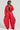 A person is dressed in an AKIRA Label Vivi outfit featuring the VIVI CROPPED PUFFER BOMBER IN RED and oversized quilted red pants. A black crop top peeks underneath, paired with sunglasses and red shoes. Their confident pose is accentuated by a neutral background.
