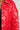 Close-up of a person wearing the VIVI Cropped Puffer Bomber in Red from the AKIRA Label, accessorized with a silver button and chain necklace, set against a plain light-colored background.