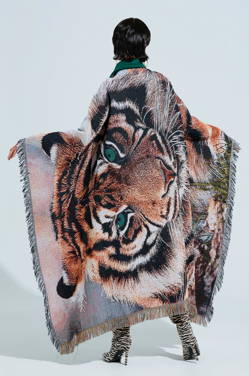 Wearing the FIRST ROUND DRAFT PICK TAPESTRY BOMBER featuring an intricate tiger design, a person stands against a plain background. The large, fringed tapestry elegantly extends over their back like a bomber jacket, paired with patterned boots, exuding bold style.