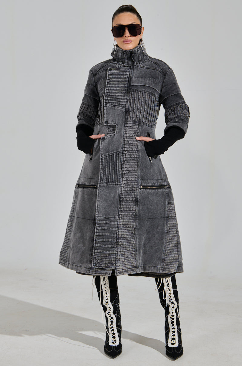 Wearing a VORTEX DENIM TRENCH COAT featuring ribbed patchwork and a high collar, paired with black and white lace-up boots, the person has sunglasses on and their hair tied back, standing against a gray background.