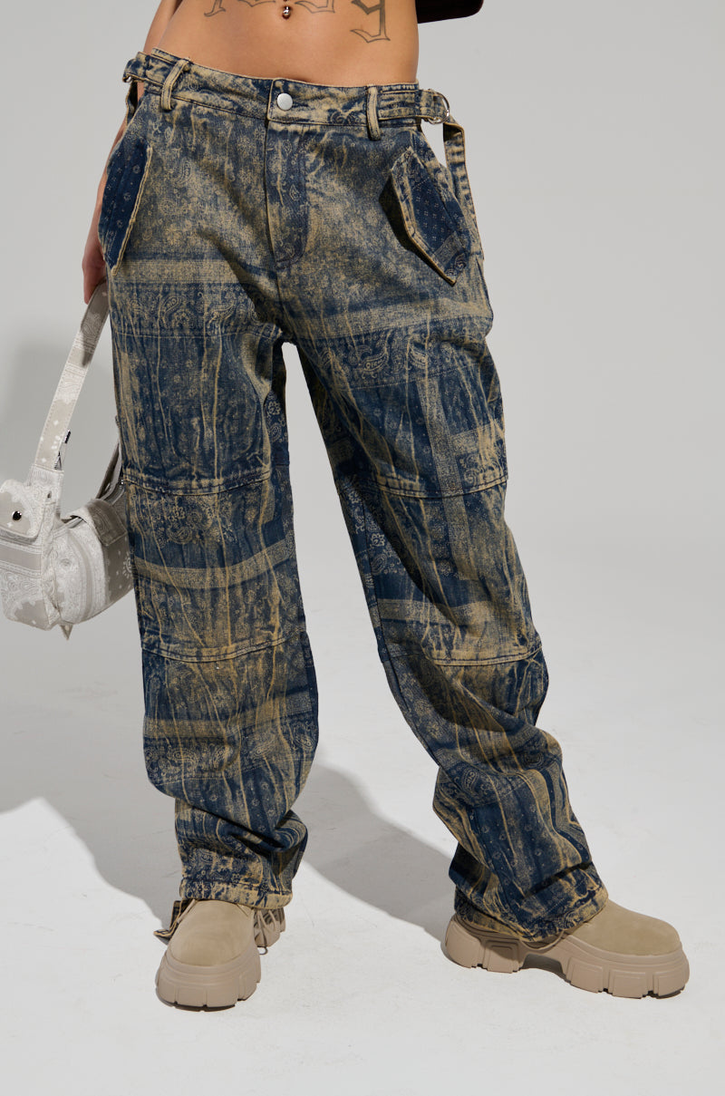 In the photo, someone is showcasing the NEVER LOSE ME DENIM PANT, featuring a high-rise wide-leg silhouette with an eye-catching acid-washed patchwork design. They complement the look with a small, light handbag and tan boots, creating an effortless urban streetwear vibe that highlights the denim's casual style.