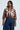 A person dressed in the GIULIA SHERPA TRIM BOMBER, featuring a brown faux leather design with white circular patterns and sherpa detailing, paired with high-waisted blue jeans. They have short, styled hair and are accessorized with hoop earrings and a gold chain necklace.