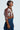 A woman in the GIULIA SHERPA TRIM BOMBER jacket, featuring a brown exterior with white sherpa trim and long ribbed sleeves, paired with high-waisted blue jeans. She stands sideways, looking forward, with short black hair and hoop earrings.