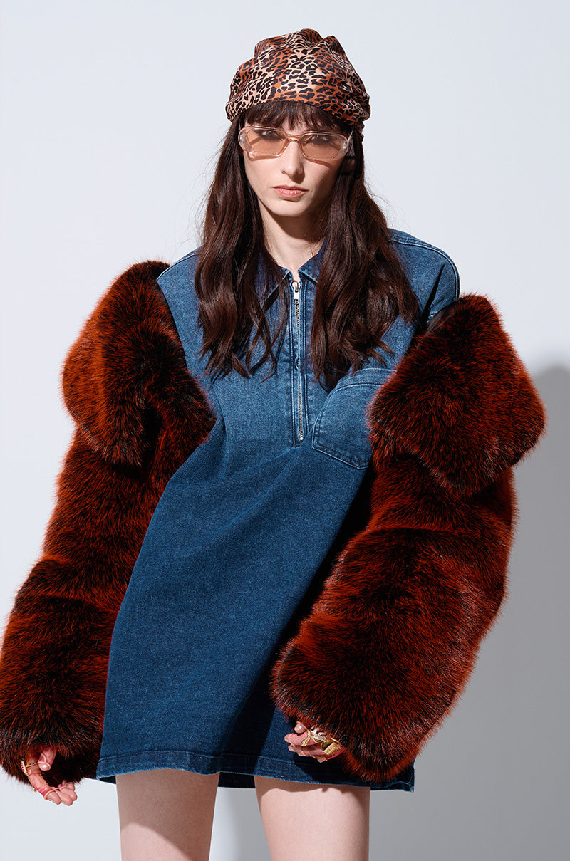A woman with long dark hair exudes a chic winter look in her blue denim dress, highlighted by the oversized red sleeves of the ALTER EGO FAUX FUR COAT. She accessorizes with a leopard print headband, sunglasses, and light-colored nail polish against a plain, light grey background.