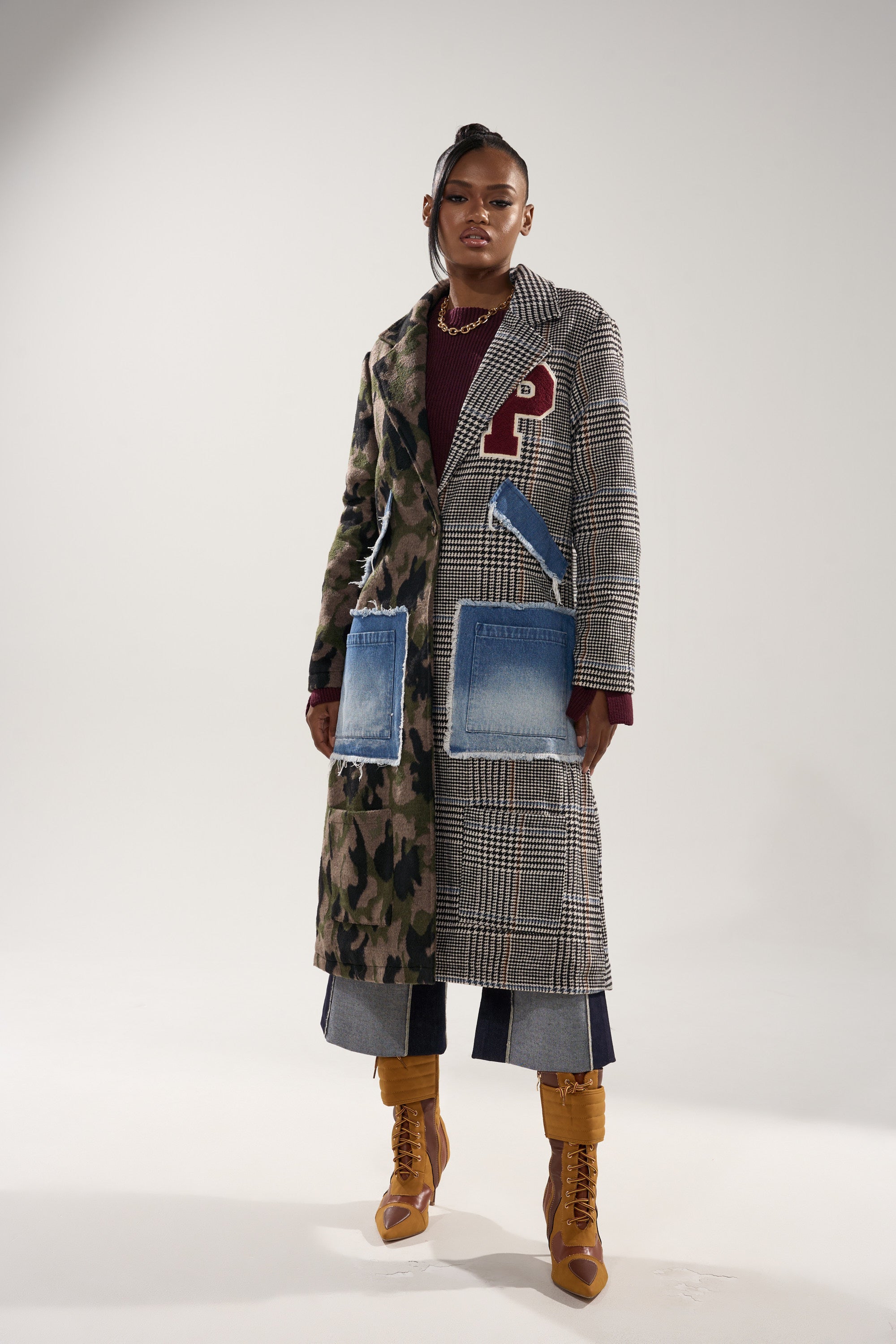 A woman stands against a plain background in the MADDIX HALF HALF TRENCH with plaid details and denim patch pockets, paired with wide-leg cropped jeans, brown boots, a burgundy top, and a bold red "P" patch.