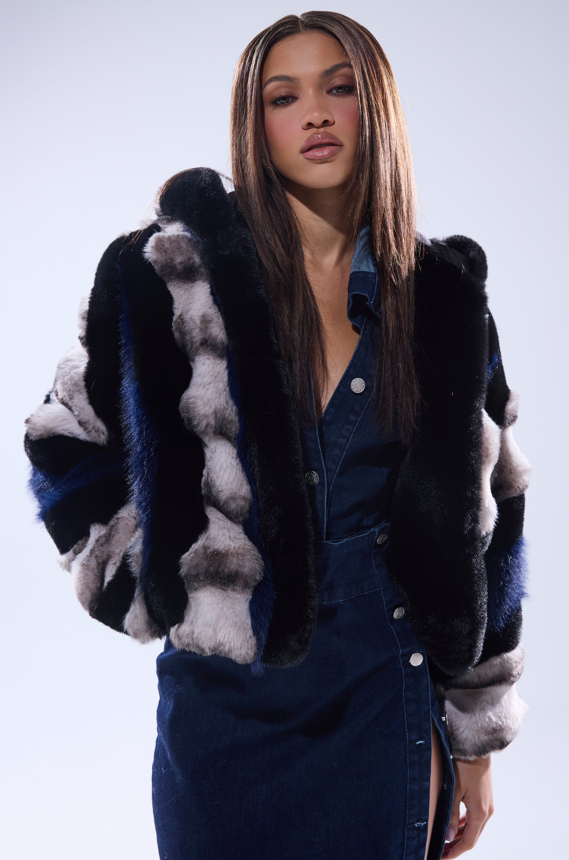 A woman with long straight hair models the SUPERNOVA PANELED FAUX FUR IN BLUE MULTI over a blue denim button-up dress, standing against a light background.