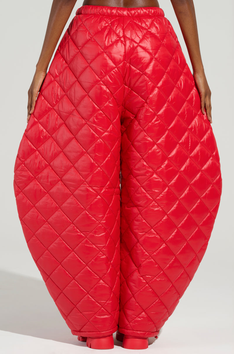 The lower half of the body is adorned in the VIVI OVERSIZED PUFFER PANTS IN RED, featuring voluminous, quilted red fabric with a glossy finish and diamond-patterned stitching against a plain background.