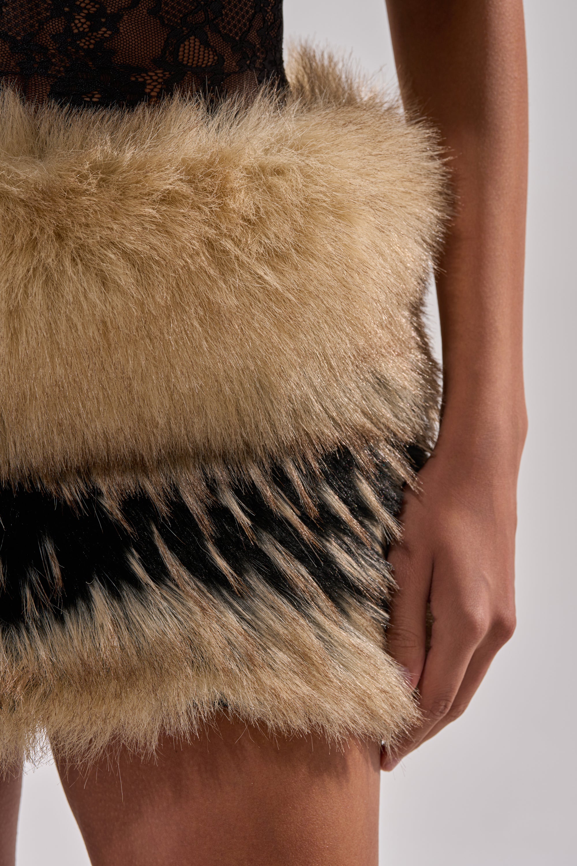 A close-up of a person wearing the COOL GIRLS ONLY LACE FUR MINI DRESS in beige and black, highlighting their arm and hand beside their body against a neutral background.