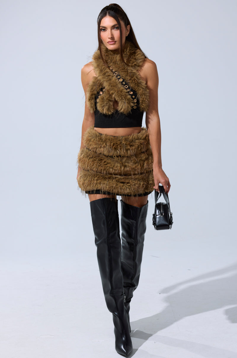 A woman exudes confidence in the WILD AND FREE FUR MINI SKIRT with a brown faux fur crop top, black over-the-knee boots, a small black handbag, and her long straight hair worn down. 6
