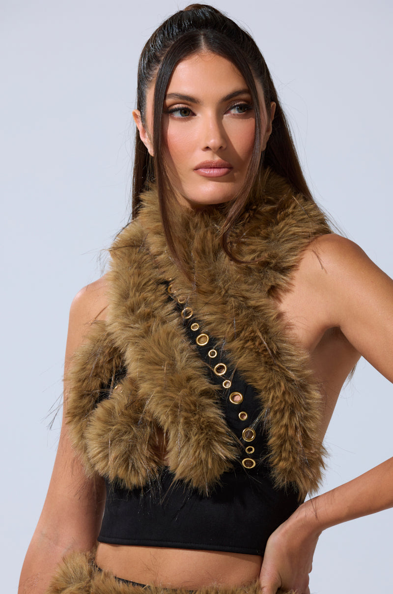 A woman with long brown hair in a ponytail wears the WILD AND FREE FUR BLOUSE—sleeveless, black, with faux fur and diagonal gold-tone detailing—set against a plain light background. 0
