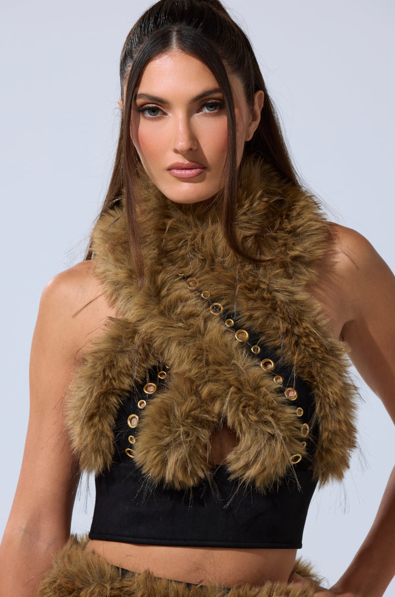 A woman with long brown hair models the WILD AND FREE FUR BLOUSE, featuring faux fur with crisscross brown accents and gold-tone grommets, against a plain light backdrop. 2