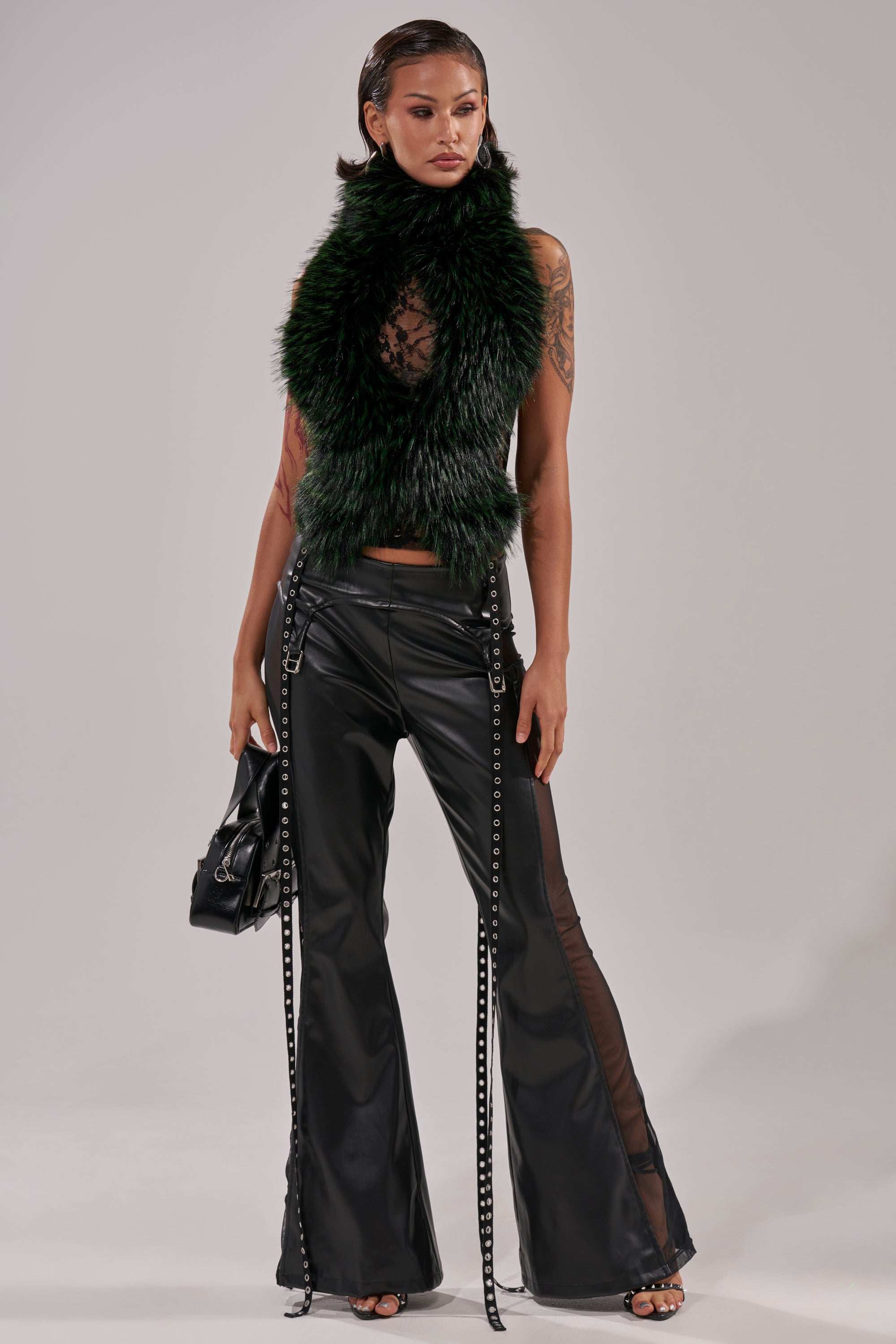 A woman poses in black leather flared pants, a sheer top, and the FEEL ME BABY FUR BLOUSE draped over her shoulders. She pairs the look with a black handbag and high-heeled sandals against a plain background.