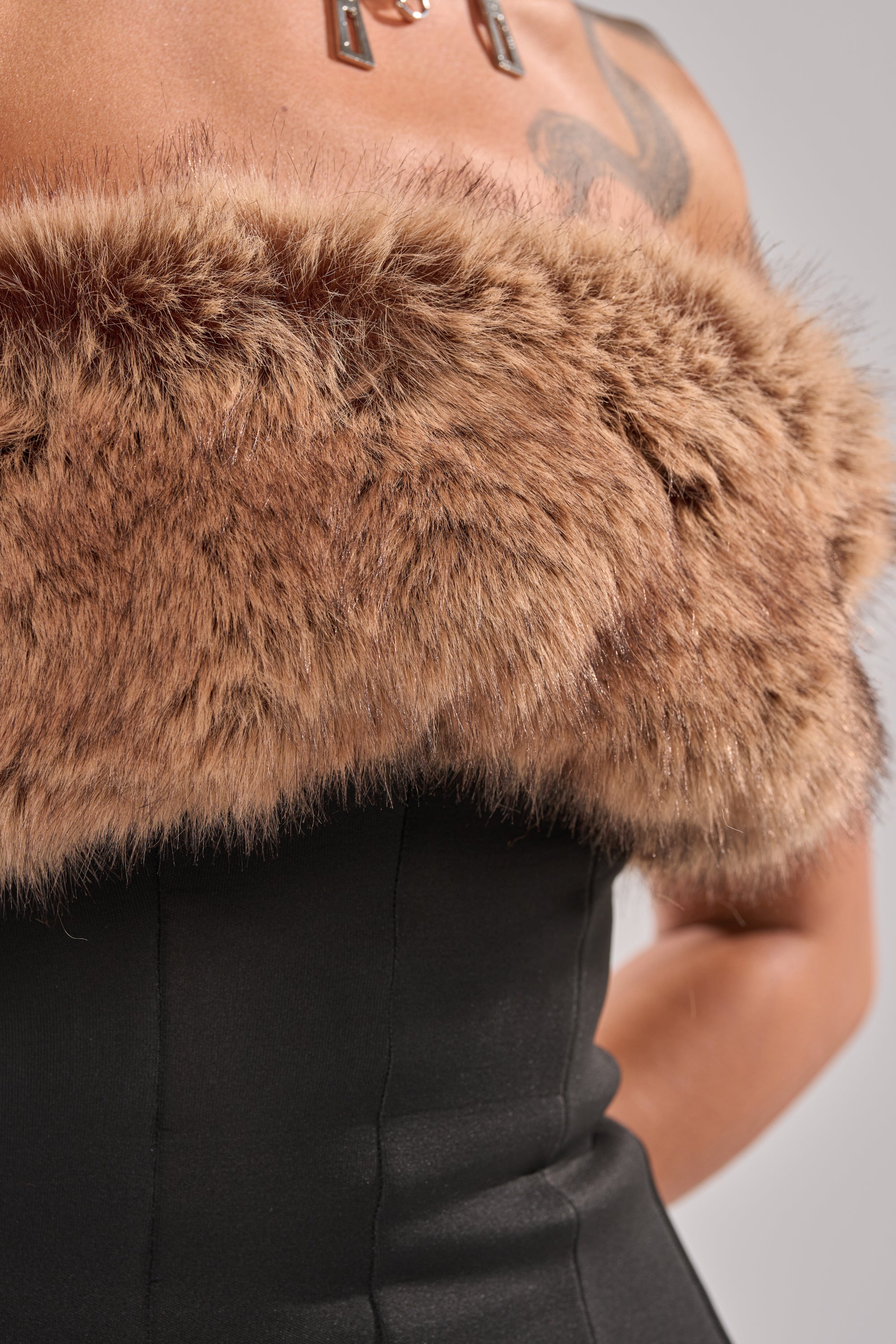A person wearing the SO CHIC FAUX LEATHER BLOUSE WITH FUR TRIM, which is strapless and black with a fur trim across the top, revealing part of their shoulder, arm, and an upper chest tattoo. 13