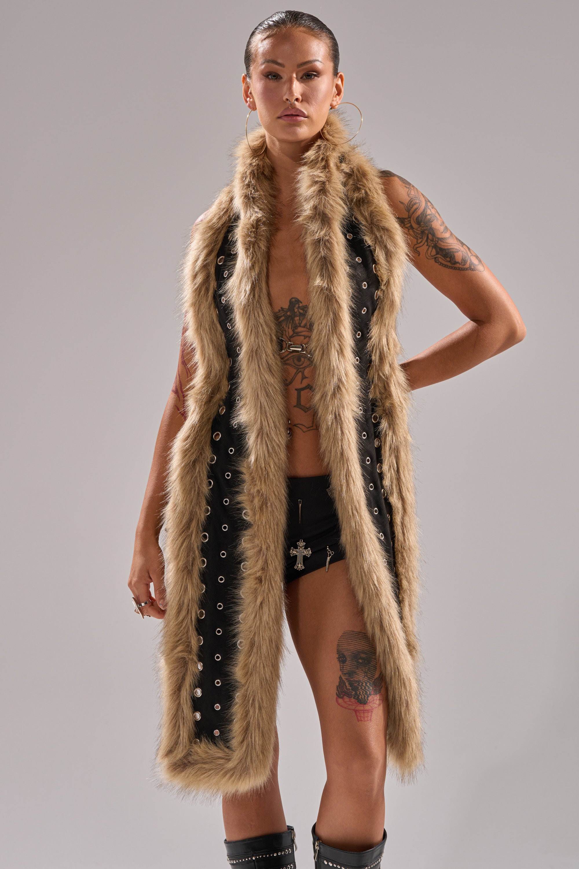 A woman with slicked-back hair models the ICY HOT FUR BRALETTE, styled with black shorts. She showcases chest, arm, and thigh tattoos while posing confidently against a plain gray background. 0