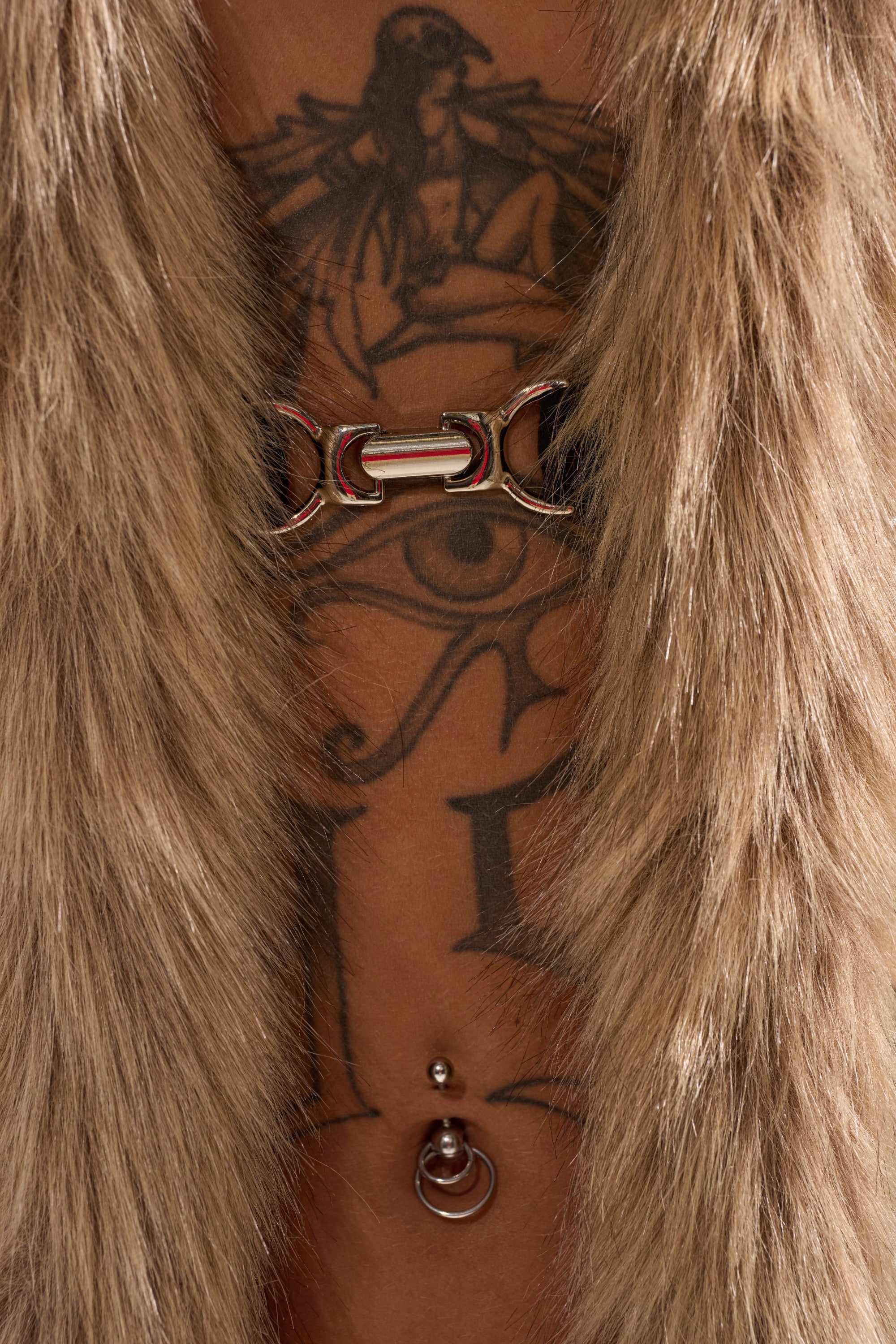 Close-up of a person's torso wearing the ICY HOT FUR BRALETTE, fastened with a metallic clasp, showcasing body piercings and a large tattoo featuring an eye and a winged figure. 8