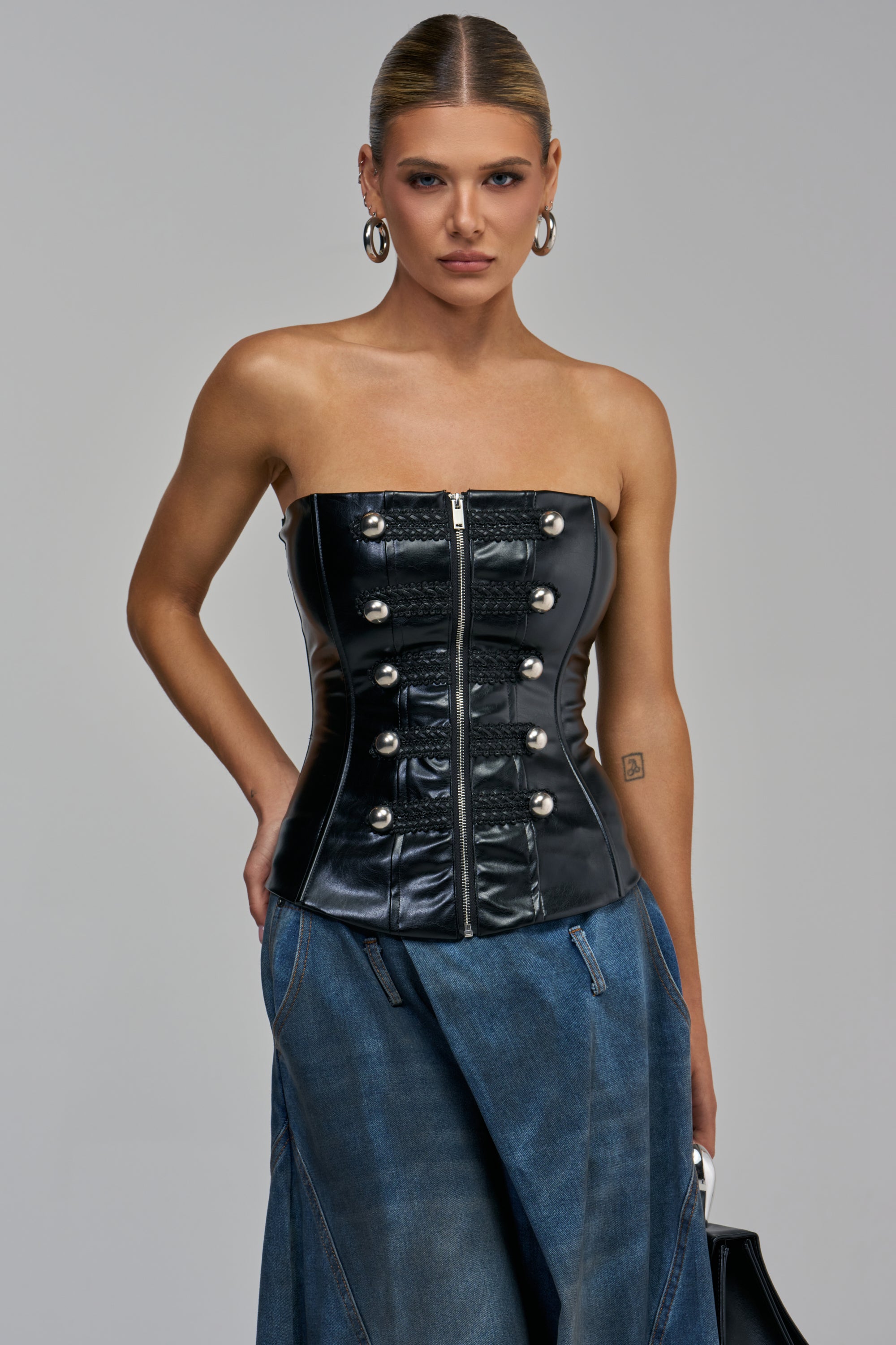 THEE BADDEST PU CORSET is a black faux leather strapless top featuring a front zipper and silver buttons for an edgy-chic look.