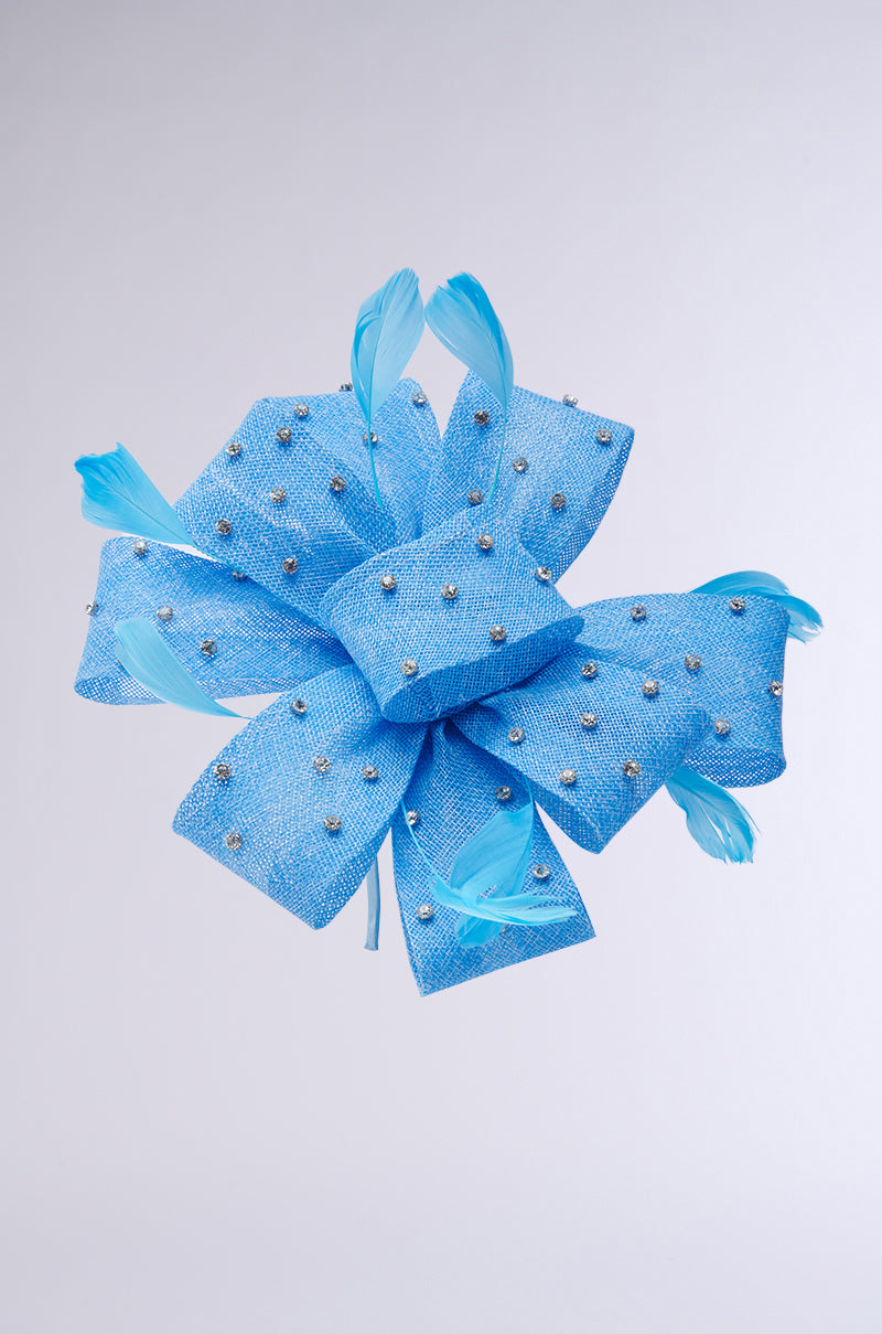 A large, decorative blue bow adorned with rhinestones and light blue feathers extends from the DENIM AND DIAMONDS CLIP ON HEADBAND. The plain, light gray background highlights its intricate details.