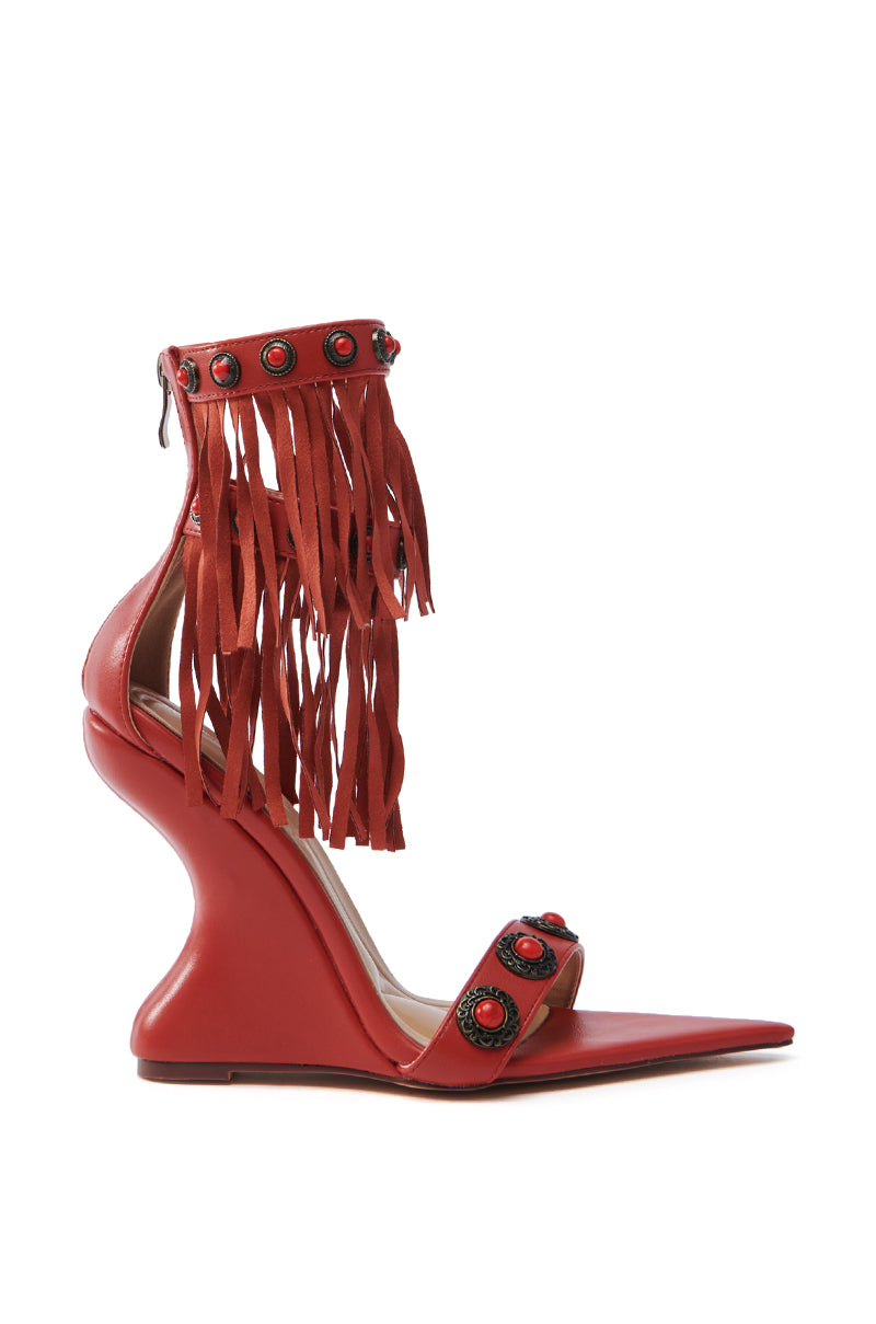 The AZALEA WANG KALILA RED FRINGE SANDAL is a festival-ready red high heel featuring a unique curved wedge, fringe, and decorative red and black circular details on the straps. It includes gemstone embellishments, a pointed toe, and a back zipper closure.