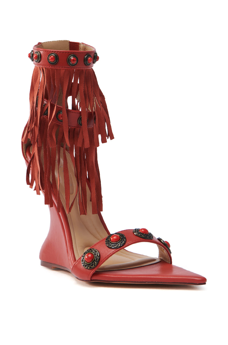 The AZALEA WANG KALILA RED FRINGE SANDAL features a pointed toe with gemstone embellishments, circular metal accents, and a high ankle strap adorned with long red leather fringes, creating a bold look perfect for standout occasions.