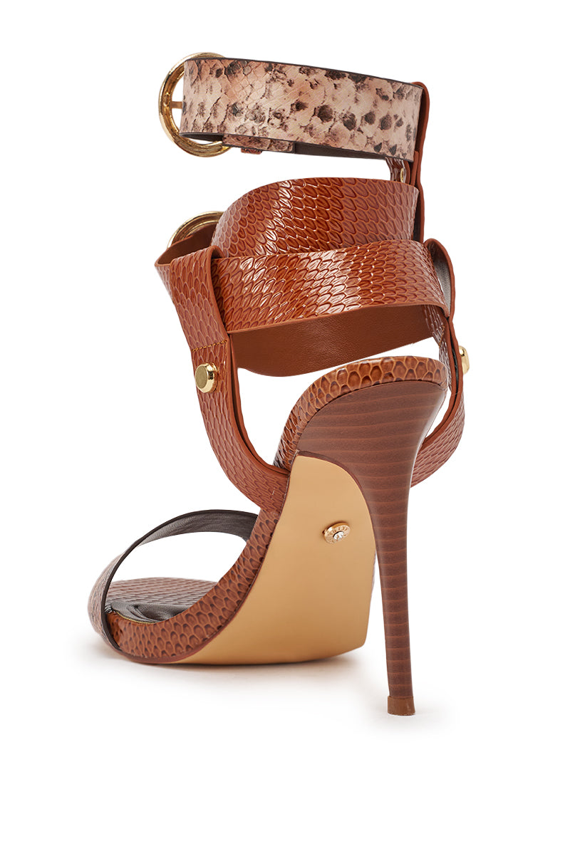 The AKIRA GOLD KADINSKY COGNAC MULTI SNAKE MATERIAL STILETTO SANDAL features snake print, gold stud accents, wide light brown buckle straps, and a comfort cushion insole—shown from the back for a stylish look with every step. 6