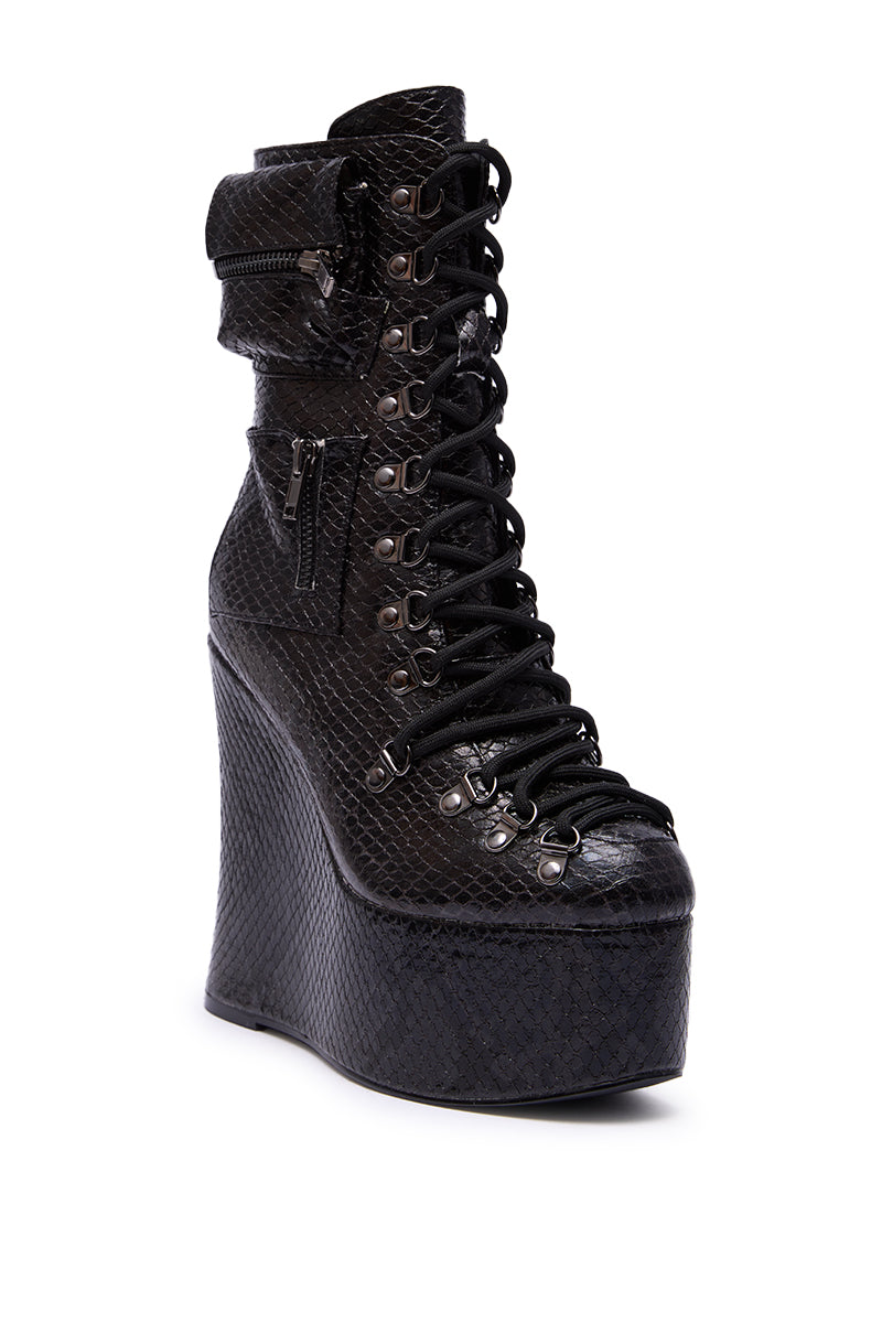 The AZALEA WANG KAPULE BLACK SNAKE PLATFORM BOOTIE features a black snakeskin pattern, lace-up front with metal eyelets, dual side zippers, and a high wedge platform sole for a bold, modern look.