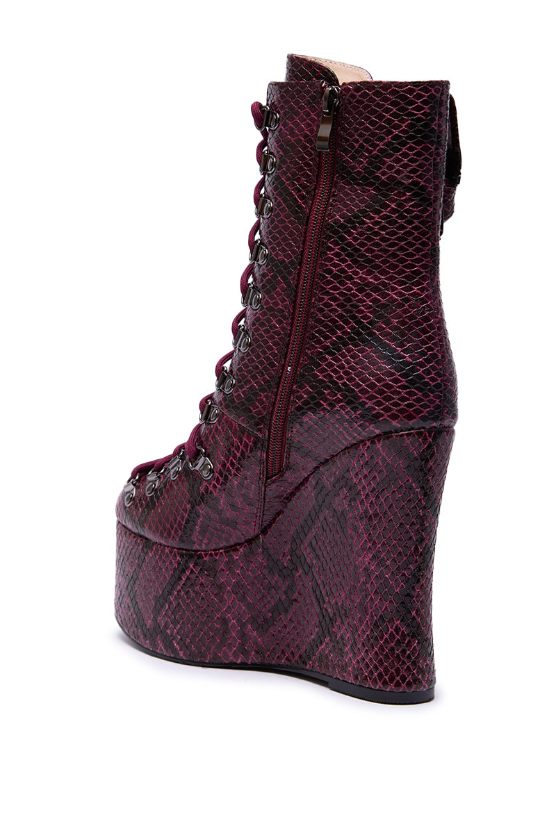 The AZALEA WANG KAPULE BURGUNDY SNAKE PLATFORM BOOTIE features a maroon and black snakeskin pattern, lace-up front, side zipper, and a high wedge heel—ideal for making a bold style statement.