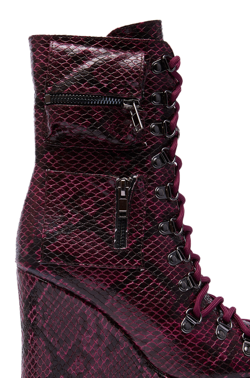 Close-up of the AZALEA WANG KAPULE BURGUNDY SNAKE PLATFORM BOOTIE, featuring a maroon and black snakeskin pattern, black laces with metal eyelets, two zippered side pockets, and a bold wedge heel.
