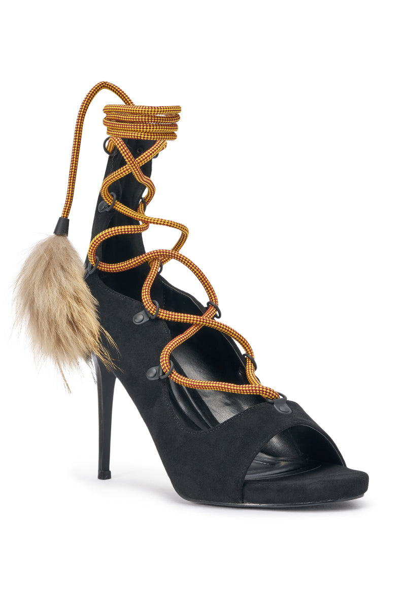 The AKIRA GOLD KARLA OLIVE FAUX SUEDE FUR EMBELLISHED STILETTO features an open toe, crisscrossing yellow and black laces, a fluffy tan fur pom-pom at the side, wraparound ankle design, and a strappy stiletto heel. 4