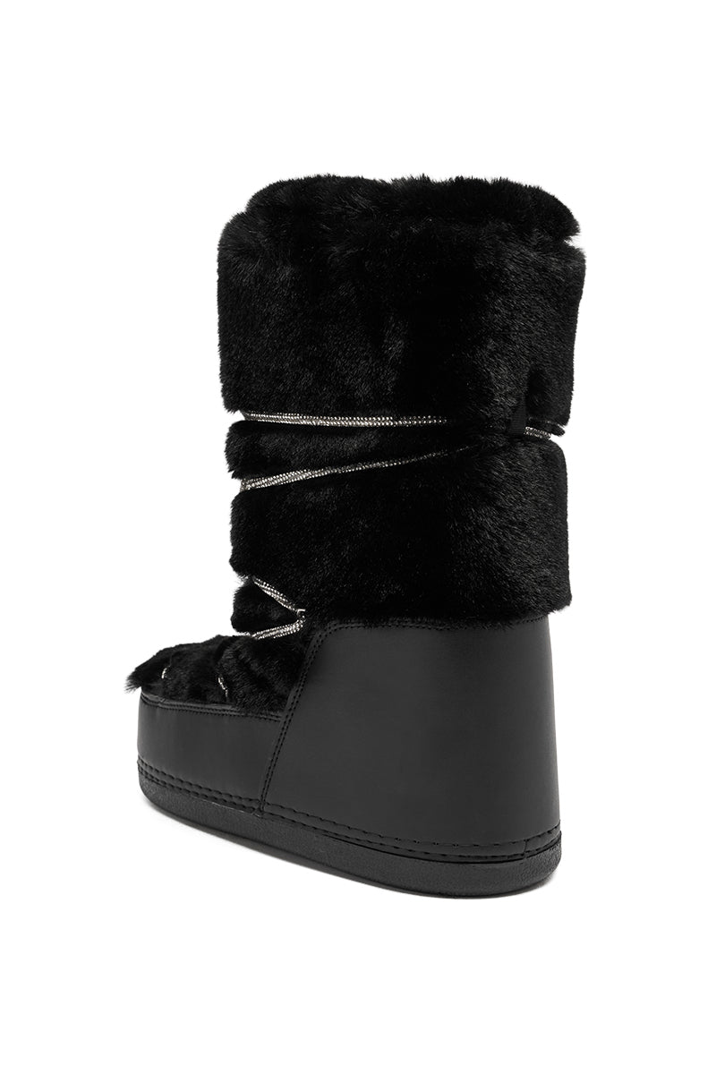 The AZALEA WANG KARMELA BLACK FUR MOON BOOT features a thick black faux fur upper, decorative laces, and a flat sole, displayed at an angle to showcase both the back and side.