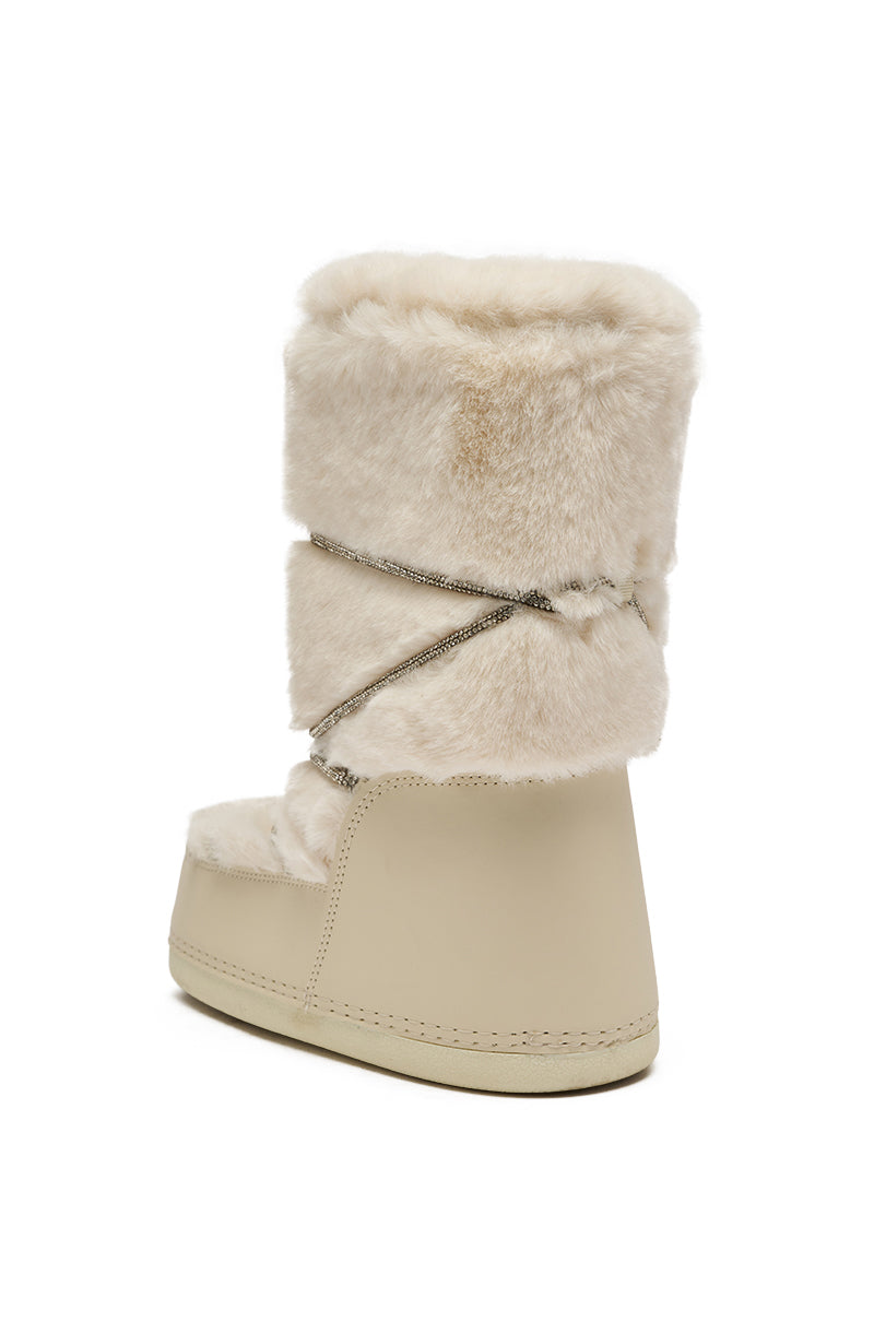 The AZALEA WANG KARMELA CREAM FUR MOON BOOT is shown from the back and side, featuring a single beige faux fur boot with a creamy upper, decorative silver cord wrap, and a solid beige rubber sole.