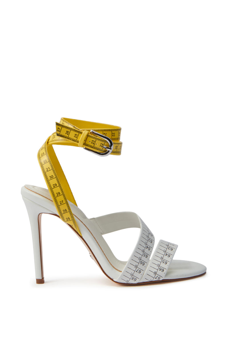 The AZALEA WANG KASHIA WHITE MULTI TAPE MEASURE STRAP SANDAL features faux leather and yellow measuring tape straps that wrap around the ankle and foot, set on a sleek stiletto heel.