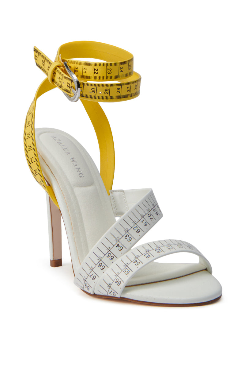 The AZALEA WANG KASHIA WHITE MULTI TAPE MEASURE STRAP SANDAL showcases faux leather white straps, a yellow measuring tape-inspired ankle strap, and a bold stiletto heel for a playful, trendy vibe.