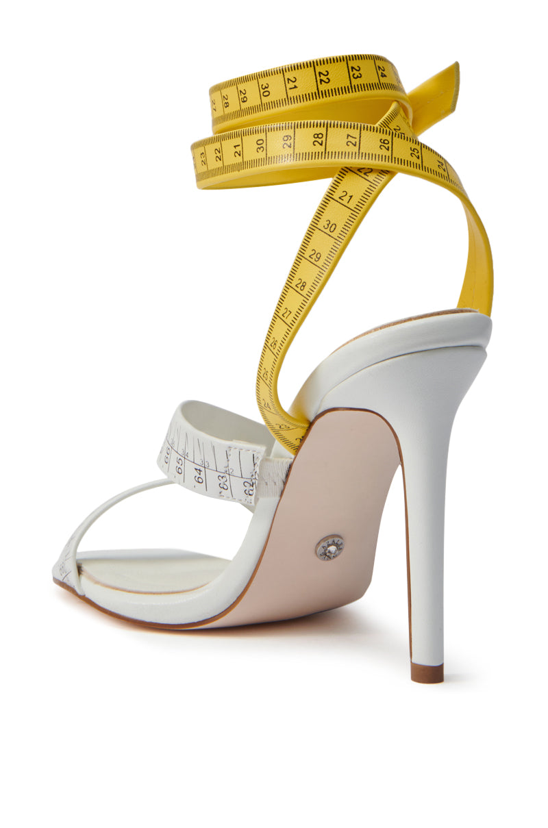 The AZALEA WANG KASHIA WHITE MULTI TAPE MEASURE STRAP SANDAL showcases yellow measuring tape straps on a crisp white base, a tall stiletto heel, and a sleek faux leather finish.