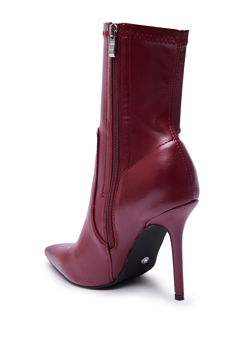 The AZALEA WANG KATHII BURGUNDY BOOTIE features faux leather, a pointed toe, side zipper, and sleek stiletto heel, shown from the back and side on a white background.