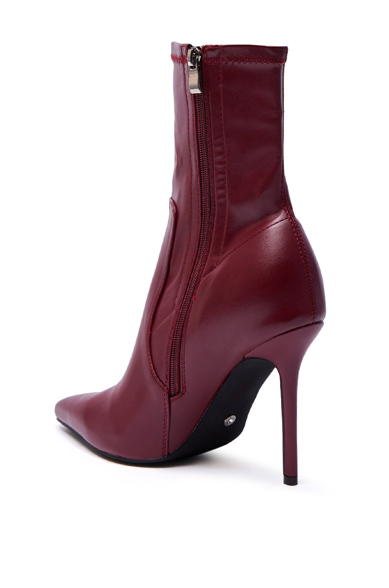A close-up of the AZALEA WANG KATHII BURGUNDY BOOTIE in glossy faux leather, featuring a pointed toe, side zipper, and stiletto heel, shown from the back and slightly to the side against a white background.