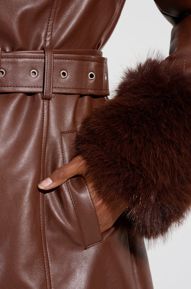 A person wearing the Kaya Fur Lined Trench in brown, featuring a matching belt and fluffy sherpa lining, has their hand in the coat pocket.