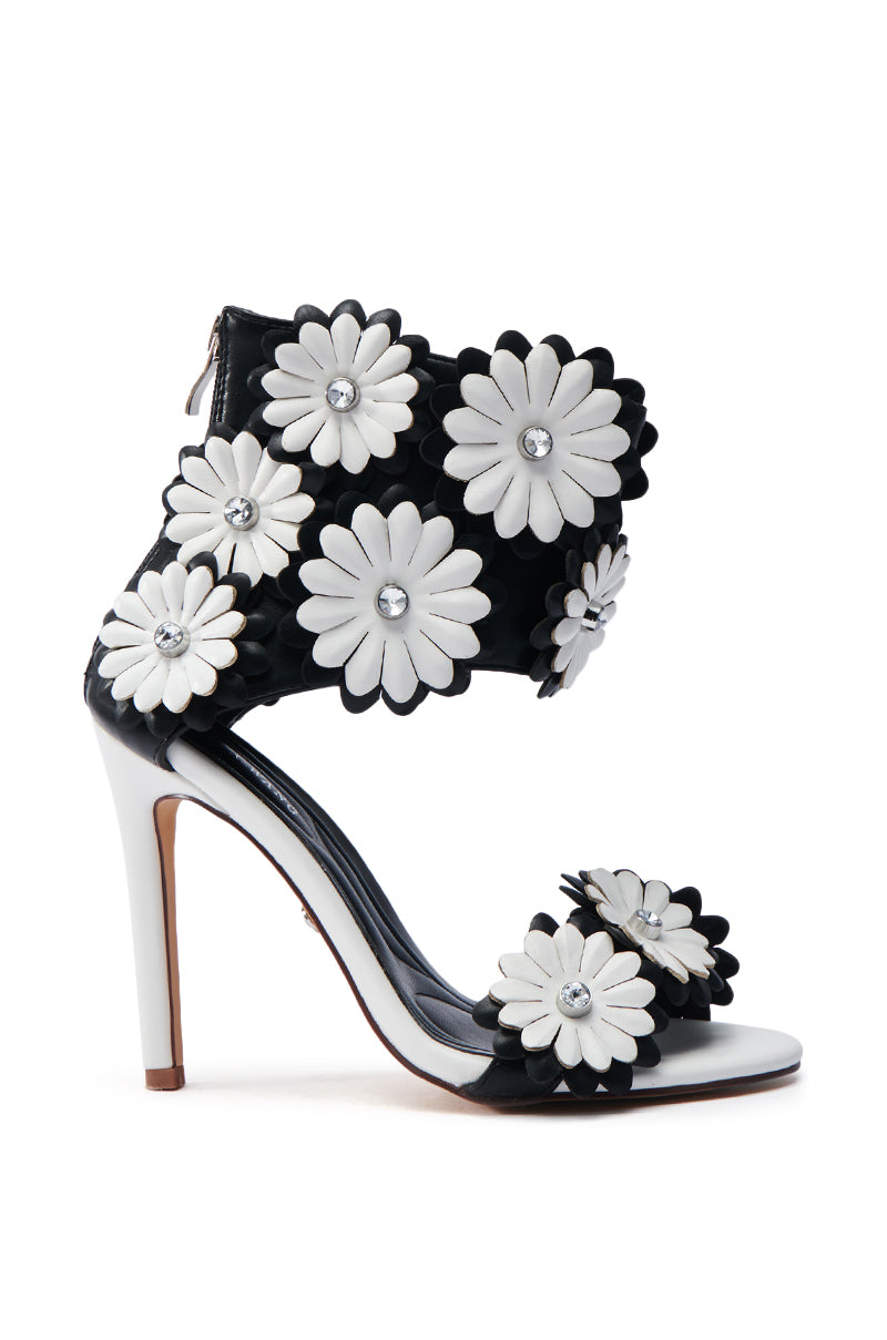 The AZALEA WANG KAYDE BLACK & WHITE STILETTO SANDAL showcases black straps adorned with 3D floral appliques of large white and black daisies with silver stud centers. Made from vegan faux leather, it includes a sleek heel and a back zipper for convenience.