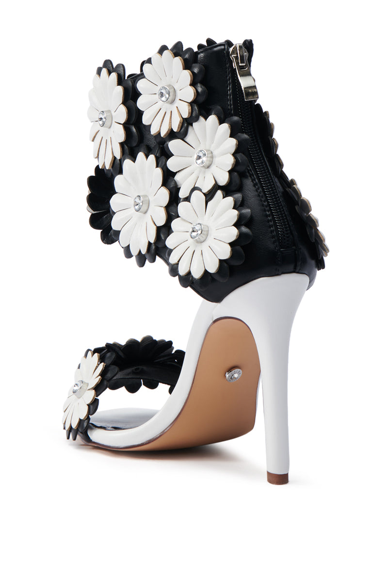 The AZALEA WANG KAYDE BLACK & WHITE STILETTO SANDAL features a striking black heel, white sole, and strap adorned with 3D floral appliques with jewel centers. Made from vegan faux leather, it also includes a handy back zipper for easy wear.