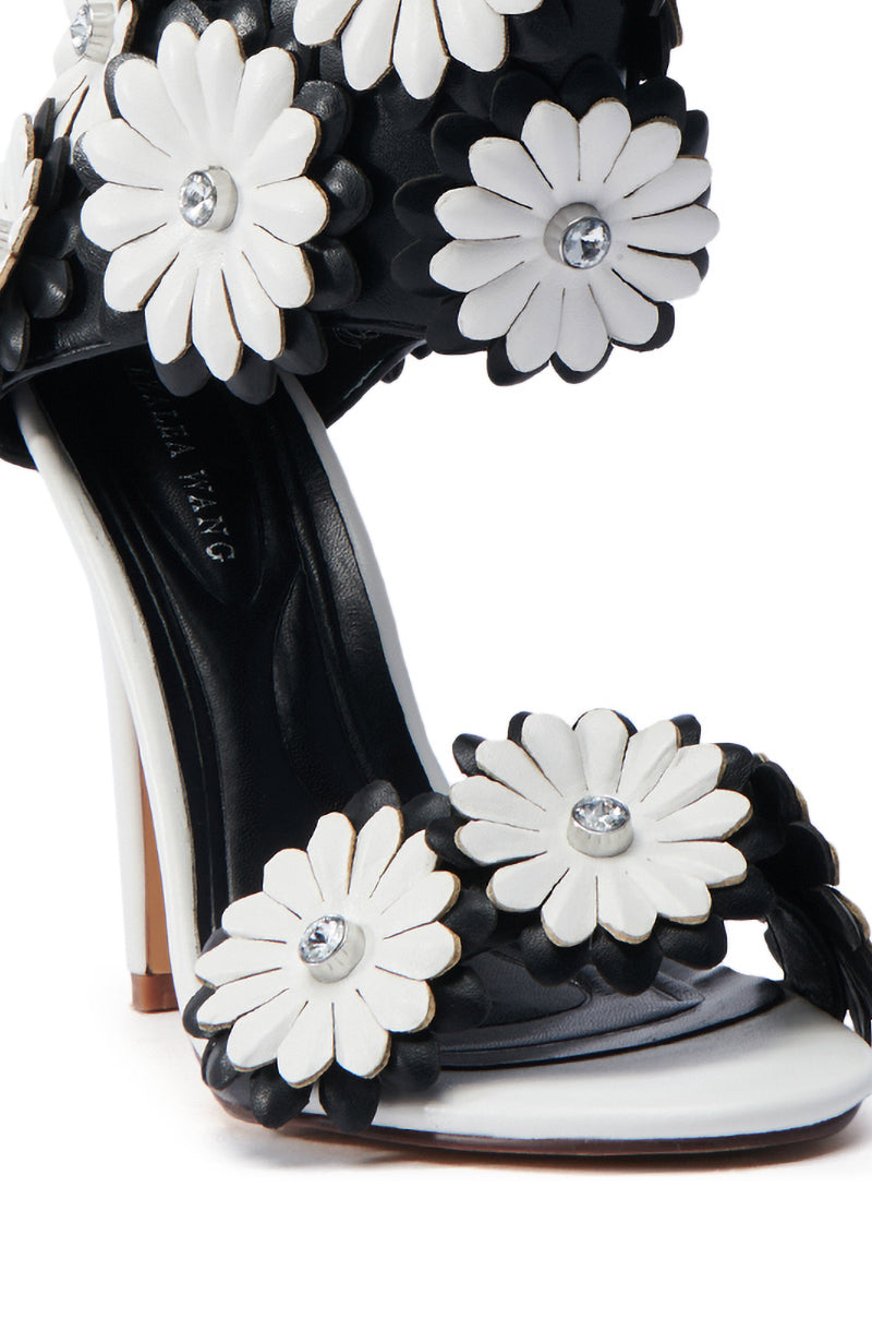 The AZALEA WANG KAYDE BLACK & WHITE STILETTO SANDAL features 3D floral appliques with rhinestone centers, crafted from vegan faux leather with a sleek black base and light tan sole.