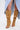 A person wears the AZALEA WANG KAZUKI TAN SLOUCHY SUEDE OPEN TOE BOOT—tan, knee-high, with large silver buttons and a stiletto heel—paired with a light blue, high-slit denim skirt against a white, minimal background.