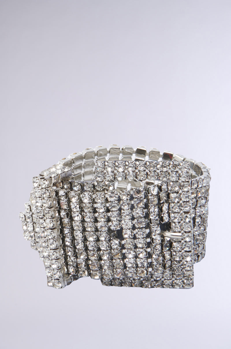 Introducing the BUCKLE UP RHINESTONE BRACELET IN SILVER: a dazzling silver accessory adorned with multiple rows of sparkling clear rhinestones. Its sophisticated design, featuring a buckled closure, exudes elegance and luxury against a plain grey background.