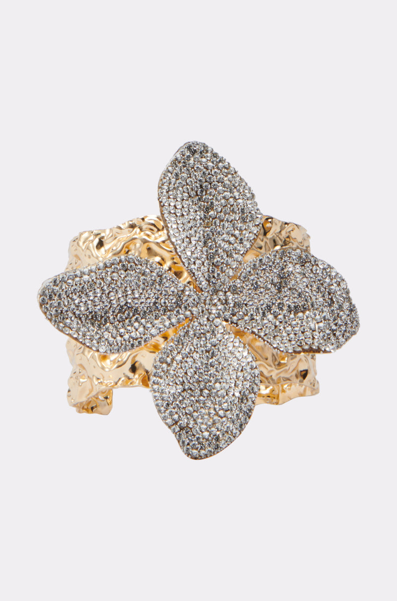 The EMI FLOWER BRACELET features a wide gold band and a sparkling flower centerpiece, with petals adorned in shimmering rhinestones for a bold, textured look. 0
