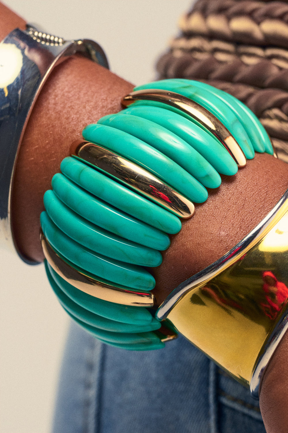 A close-up of a person's wrist shows three stacked bracelets: a sleek gold metallic bracelet, the DISC BRACELET IN TURQUOISE featuring alternating turquoise and gold-tone curved segments, and a plain, polished gold-tone cuff. This boho-chic jewelry combination creates a stylish and eye-catching statement.
