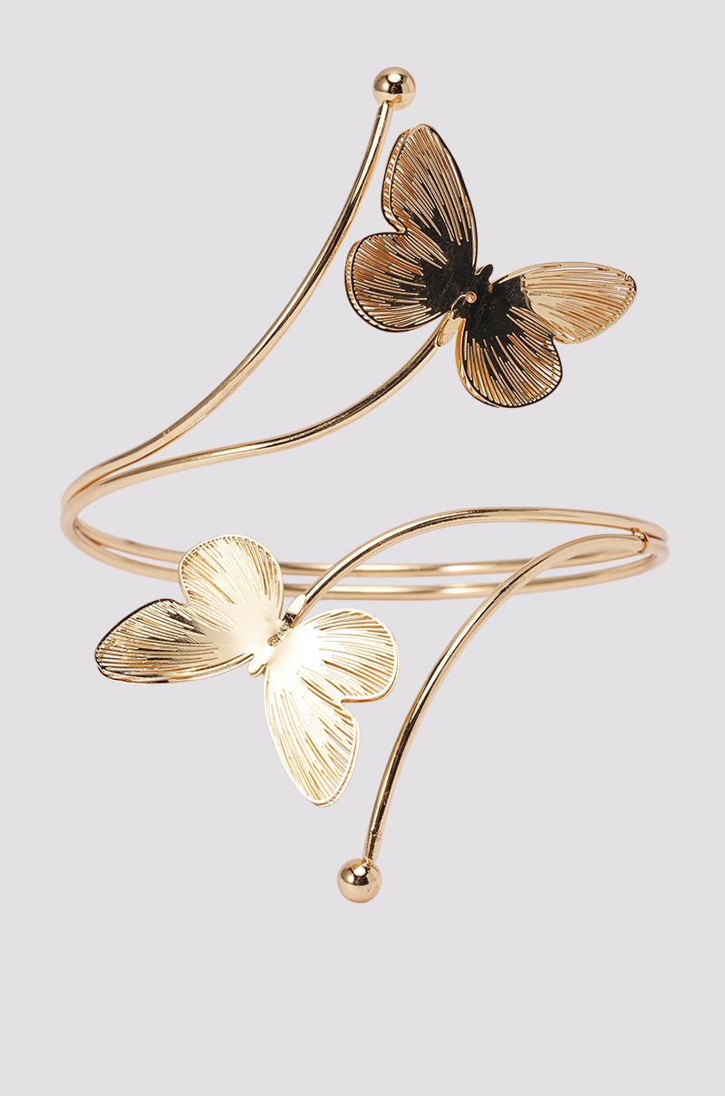 The BUTTERFLY ARM CUFF is a gold arm cuff with two textured butterflies and slim curved bands tipped with gold spheres, creating striking festival jewelry. Photographed against a light gray background.