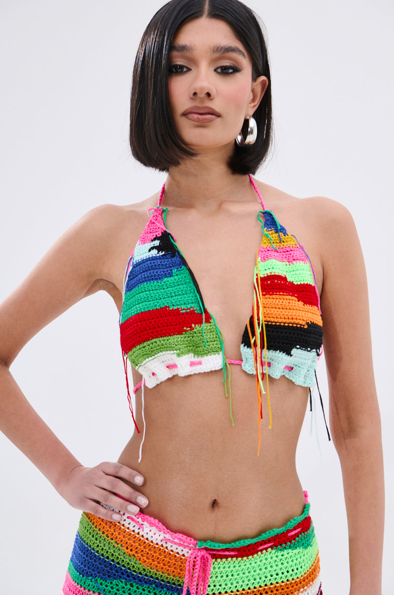 A woman with a sleek bob wears the MULTI COLORED HEART CROCHET BRA TOP, its vibrant stripes and abstract patterns highlighting her colorful, festival-ready style as she poses confidently against a plain white background.