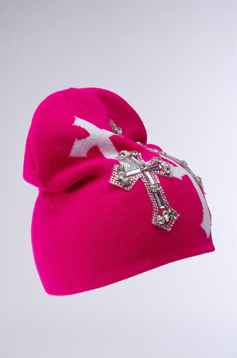 The CROSS LOVE BEANIE, a vibrant pink accessory, features decorative crosses, including a religiously-inspired cross enhanced with gems and silver rhinestones, set against a simple background. 2