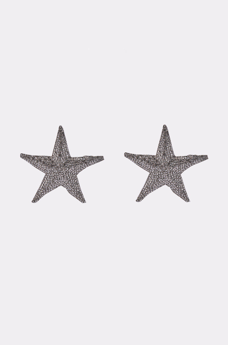 The IBIZA EARRING is a pair of glittery, silver, rhinestone star-shaped earrings displayed on a plain white background. 1