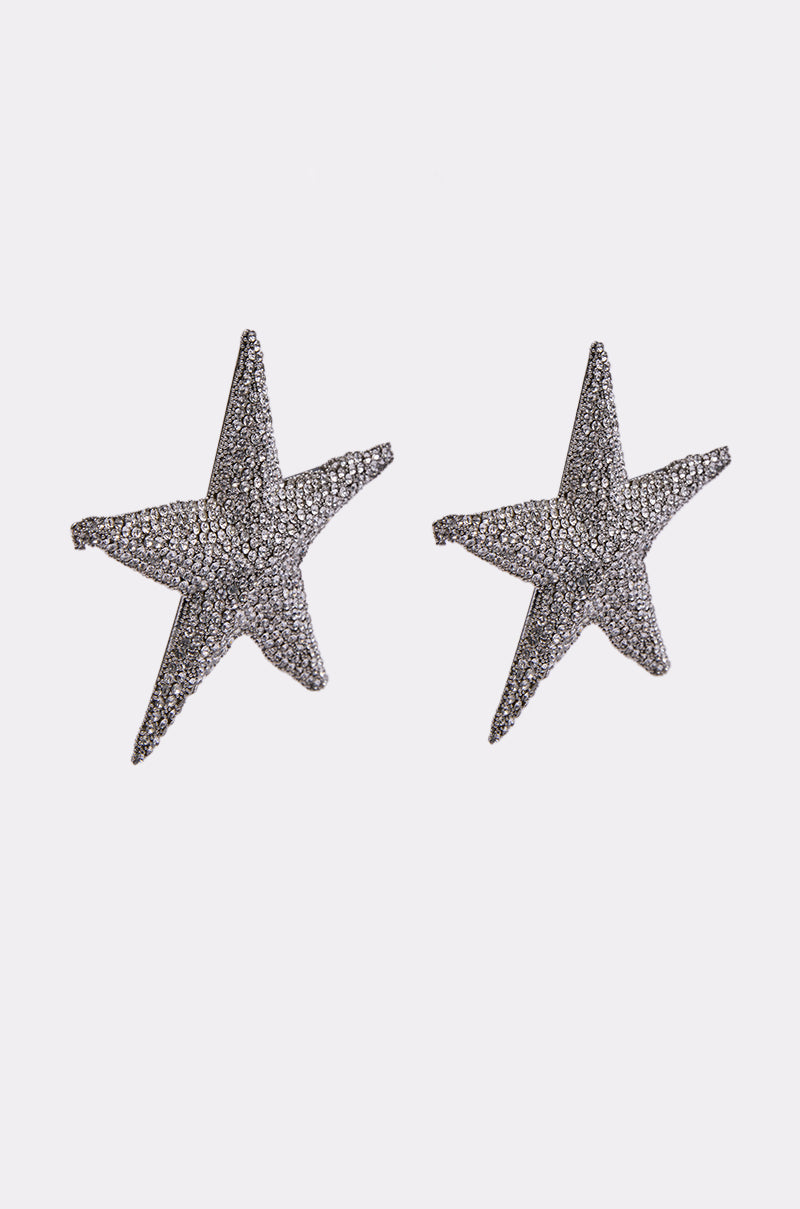 The IBIZA EARRING is a pair of silver, star-shaped earrings with sparkling rhinestone accents, shown on a plain white background. 3