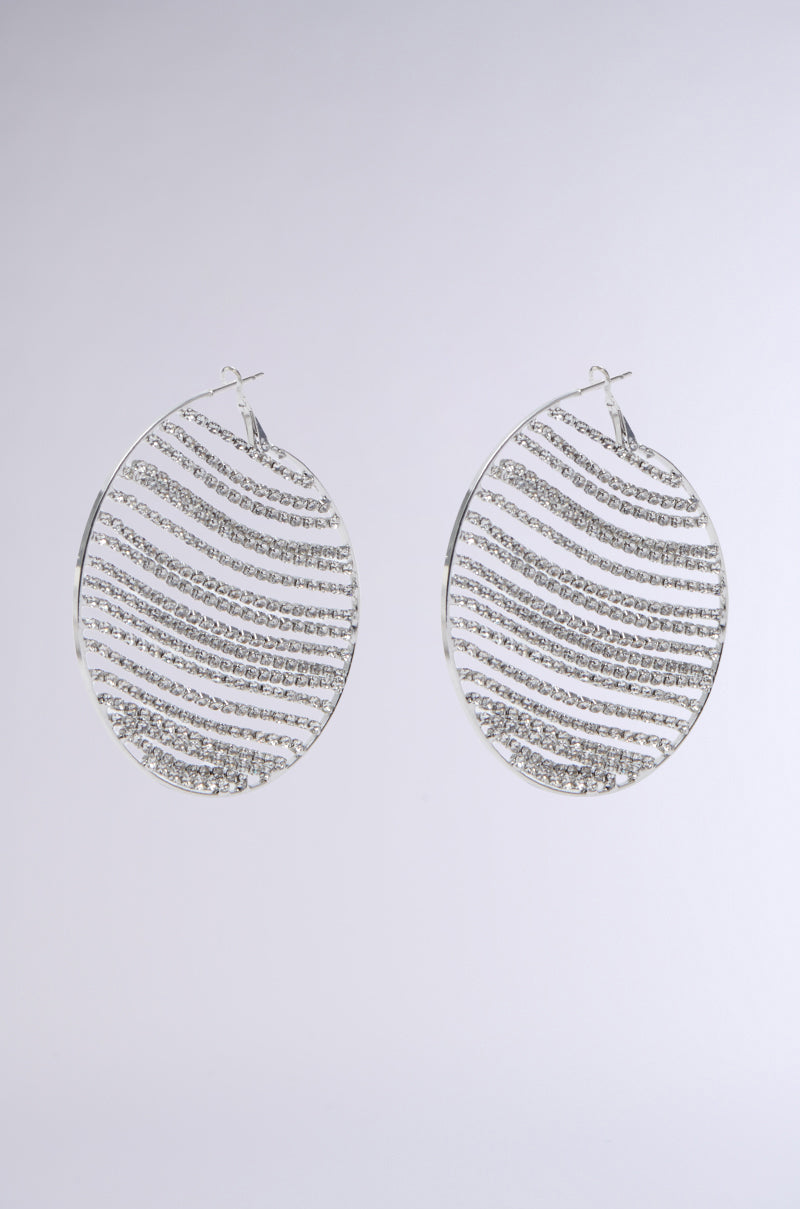 The MAIN MOMENT BLING HOOP EARRING showcases an oval shape with a metallic base, featuring alternating smooth and textured silver stripes against a plain white background.